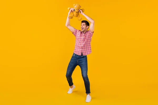 Foto de cuerpo completo del hombre feliz positivo levantar juguete oso buen humor buscar espacio vacío aislado en el fondo de color amarillo —  Fotos de Stock