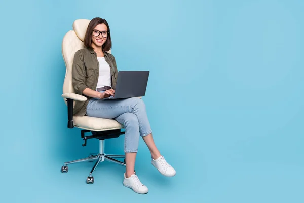 의자에 앉아 있는 여성의 전신 사진은 전자 우편 문자 메시지를 입력하는 장치를 사용하여 파란색 배경에 분리 된 카키 데님 옷을 입는다 — 스톡 사진