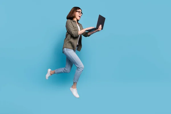 Profilo completo del corpo foto laterale del computer nerd signora salto utilizzare dispositivo chattare usura camicia jeans denim isolato su sfondo di colore blu — Foto Stock