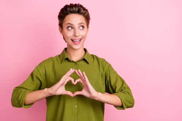 Foto de señora loca dedos muestran símbolo del corazón mirada espacio vacío desgaste camisa verde aislado color rosa fondo —  Fotos de Stock