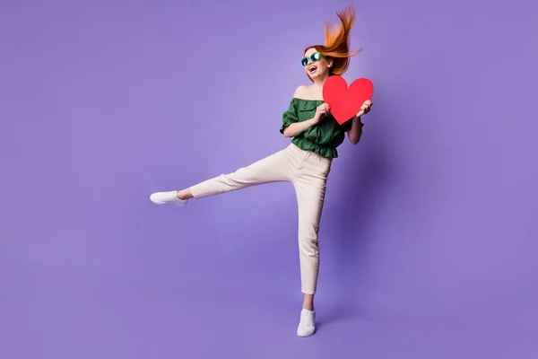 Full size photo of funny ginger hair young lady dance with heart wear glasses green bare shoulders blouse trousers isolated on violet background — стоковое фото