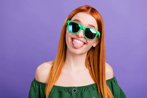 Photo of cute childish young lady wear green blouse dark glasses smiling showing tongue isolated purple color background — 图库照片