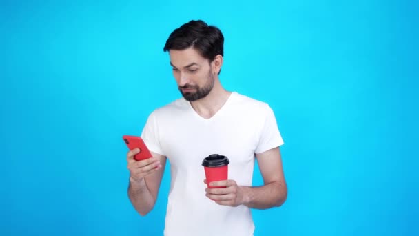 Guy resto frio bebida latte uso telefone inteligente isolado no fundo de cor azul — Vídeo de Stock