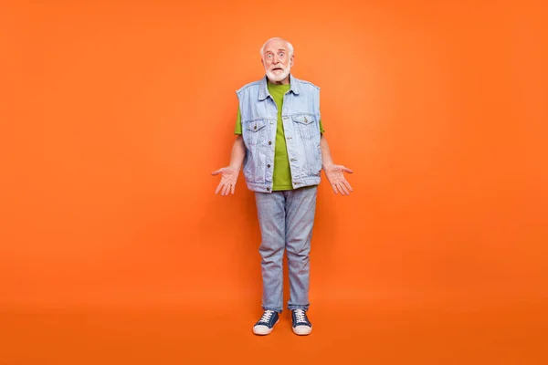 Photo of impressed unsure man pensioner dressed retro denim vest not knowing answer shrugging shoulders isolated orange color background