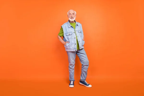 Foto de hermoso encantador hombre retirado usar jeans vintage chaleco caminando sonriente aislado color naranja fondo —  Fotos de Stock