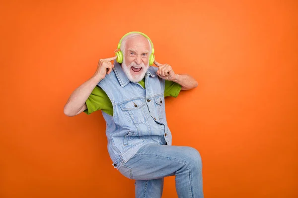 Фото фанкі крутого чоловіка на пенсії в старовинному джинсовому жилеті, що слухає музичні навушники, що співають усміхнений ізольований помаранчевий колір фону — стокове фото