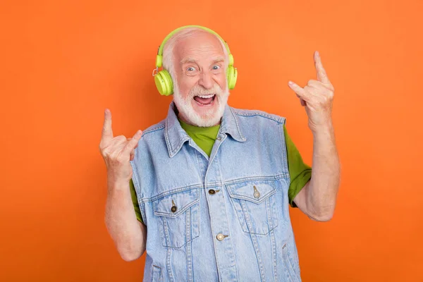 Фото смішного божевільного чоловіка пенсіонера, одягненого в ретро джинсовий жилет навушники, посміхаючись показуючи хард-рок знак ізольований помаранчевий колір фону — стокове фото