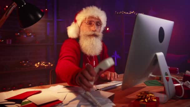 Veselý zodpovědný Santa sedět stůl psaní klávesnice mají telefonní hovor — Stock video