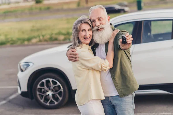 Photo of happy wife husband old people new car keys hug enjoy good mood smile parking outside outdoors in city