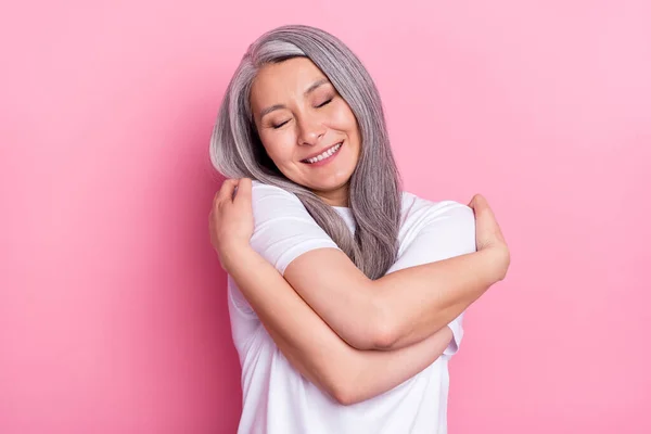 Portret van aantrekkelijke vrolijke dromerige blij grijs-harige vrouw knuffelen zichzelf geïsoleerd over roze pastel kleur achtergrond — Stockfoto