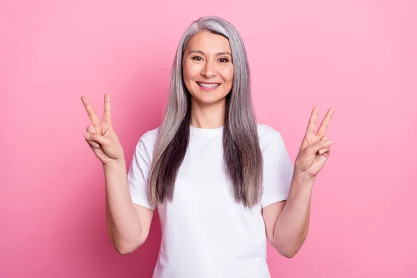 Foto portrét stárnoucí ženy ukazující mír V-znak usmívající se izolované na pastelové růžové pozadí — Stock fotografie