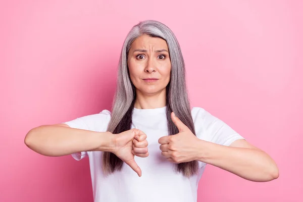 Photo portrait of aged woman showing thumb up down unsure doubt isolated on pastel pink color background — Stockfoto