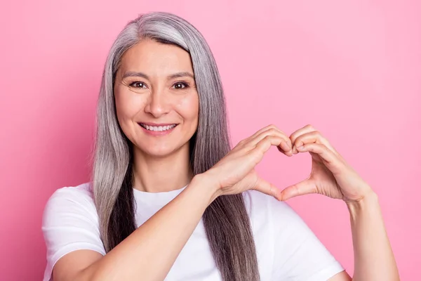 Photo portrait of aged woman with grey hair showing heart shaped gesture isolated on pastel pink color background — Fotografia de Stock