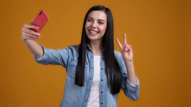 Lady maken selfie smartphone sturen kus vsign geïsoleerde oranje kleur achtergrond — Stockvideo