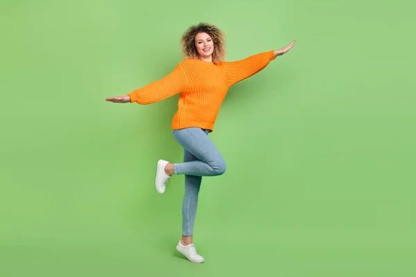 Full size foto van cool blond golvend kapsel dame vliegen dragen oranje pullover jeans sneakers geïsoleerd op groene kleur achtergrond — Stockfoto