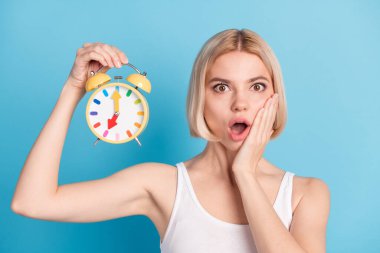Portrait of worried lady arm on cheek open mouth hold classic clock look camera isolated on blue color background clipart