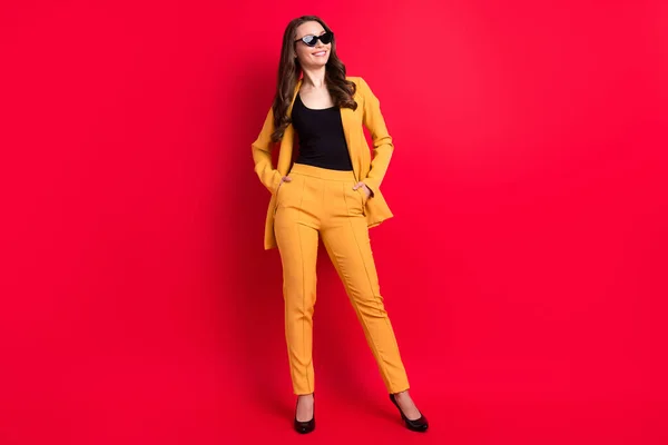 Fotografie okouzlující legrační dáma oblečená žluté sako tmavé brýle usmívající se ruce kapsy prázdný prostor izolované červené barvy pozadí — Stock fotografie