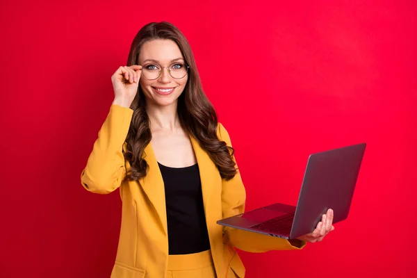 Портрет привлекательной веселой девушки, держащей в руках ноутбук касаясь спецификации изолированы на ярко-красном фоне — стоковое фото