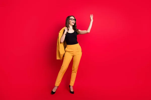 Fotografie hezké okouzlující mladá žena nosit žluté bundy brýle mávání rameno prázdný prostor s úsměvem izolované červené barvy pozadí — Stock fotografie
