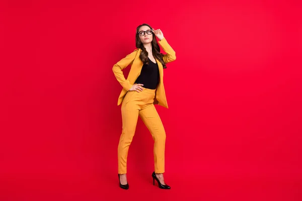 Foto de confiado fresco joven dama vestida amarillo blazer gafas brazo cintura buscando espacio vacío aislado color rojo fondo —  Fotos de Stock