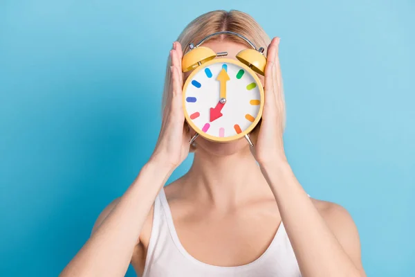 Foto da jovem mulher segurar relógio alarme tampa close face desgaste singlet gestão do tempo isolado no fundo de cor azul — Fotografia de Stock