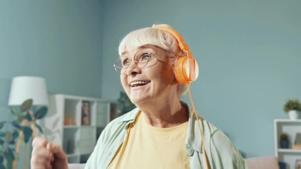 Беззаботный положительный смешной бабуля танцы носить наушники слушать музыку — стоковое видео