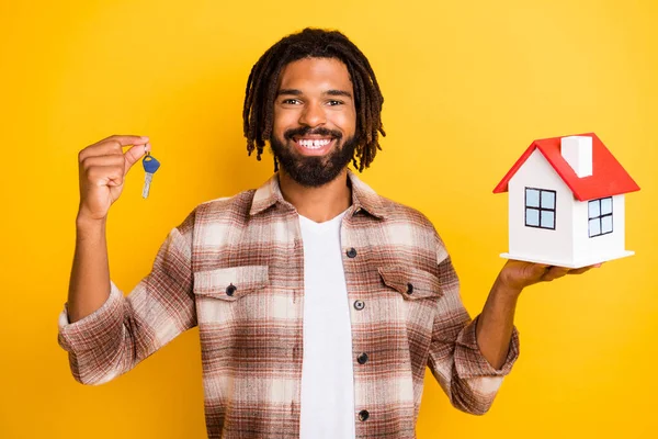 Portrait photo d'un homme brunet montrant une maison en papier souriant gardant la clé de nouveaux appartements isolés sur un fond de couleur jaune vif — Photo