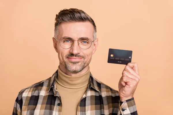 Foto van volwassen man houden bankpas inkomen cashless adverteren raden geïsoleerd over beige kleur achtergrond — Stockfoto