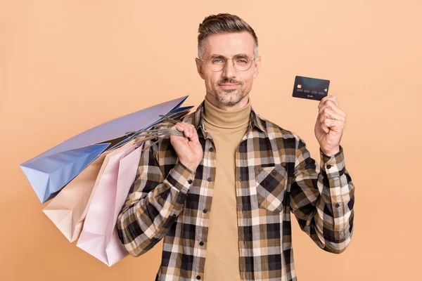 Foto van volwassen man blij hold pakket koopje debetkaart transactie salaris winkelcentrum geïsoleerd over beige kleur achtergrond — Stockfoto