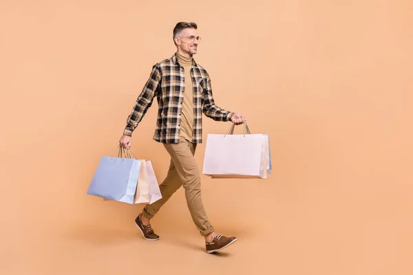 Full size profiel zijkant foto van volwassen man hold tas lopen kijken lege ruimte boetiek geïsoleerd over beige kleur achtergrond — Stockfoto