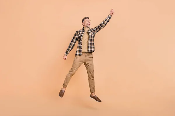 Full size photo of mature man jump up try to catch umbrella look empty space isolated over beige color background — Stock Photo, Image
