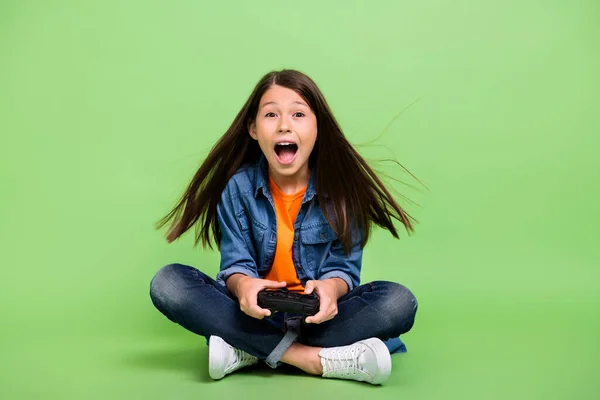 Full length foto van cool klein meisje play station schreeuwen dragen shirt jeans schoenen geïsoleerd op groene achtergrond — Stockfoto