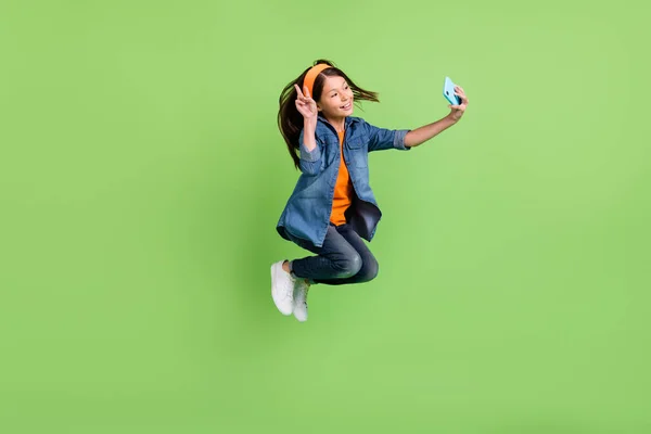 Полноразмерная фотография профиля крутой маленькой девочки прыгать делать селфи носить джинсовые туфли с обручем изолированные на зеленом фоне — стоковое фото