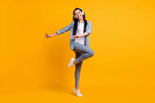 Foto em tamanho completo de cool otimista morena senhora ouvir música dança desgaste azul camisa jeans tênis isolado no fundo de cor amarela — Fotografia de Stock