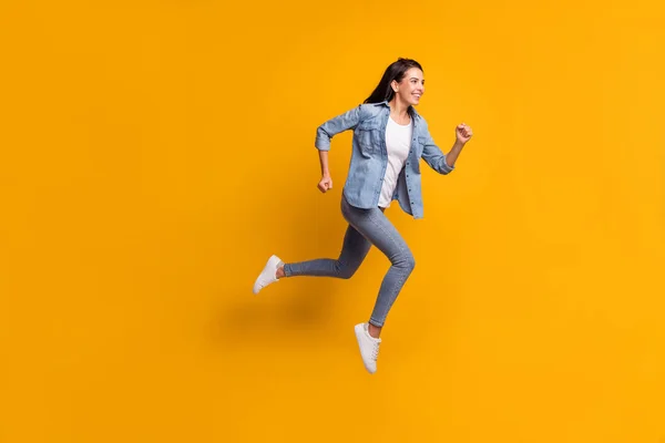 Full size profiel foto van cool optimistische brunette dame run jump wear blauw shirt jeans sneakers geïsoleerd op gele kleur achtergrond — Stockfoto