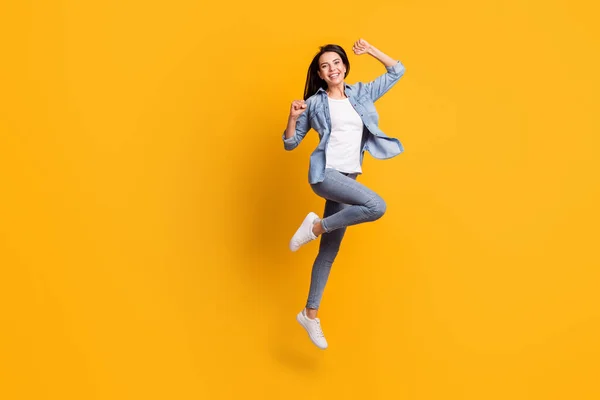 Full size profiel foto van cool hoera brunette dame run springen dragen blauw shirt jeans sneakers geïsoleerd op gele achtergrond — Stockfoto