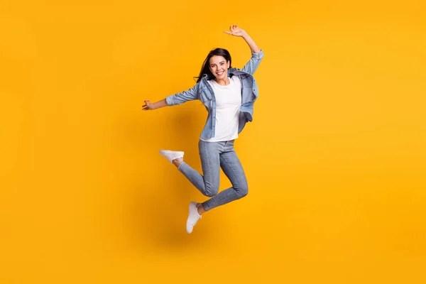 Full size profiel foto van cool optimistische brunette dame springen dragen blauw shirt jeans sneakers geïsoleerd op gele achtergrond — Stockfoto