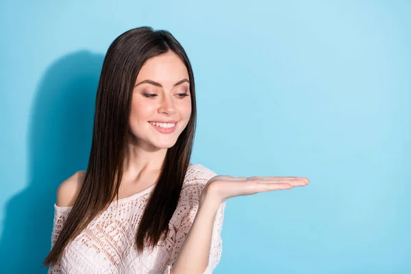 Foto de encantadora mujer joven positiva mira de la mano vacío espacio producto aislado sobre fondo de color azul — Foto de Stock