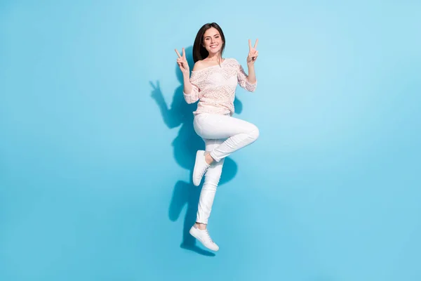 Celá tělo fotografie šťastný pěkný pozitivní mladá žena, aby v-značky cool skok do vzduchu izolované na modrém pozadí — Stock fotografie