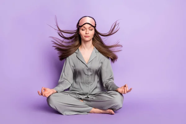 Foto de cuerpo entero de mujer tranquila sentada en pose de loto practicando yoga aislado sobre fondo de color violeta pastel —  Fotos de Stock