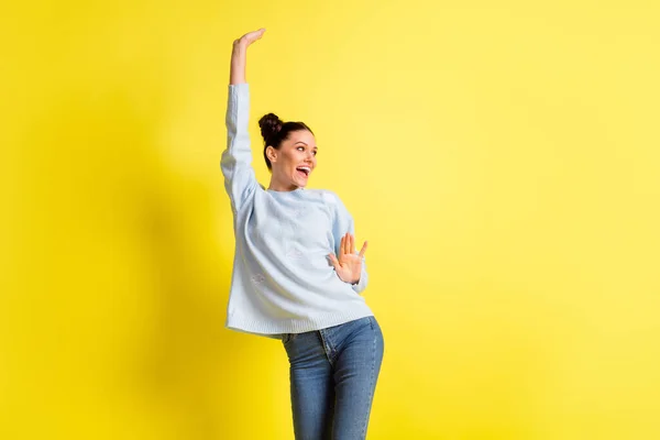 Foto de señora alegre levantar la mano mirada espacio vacío desgaste pantalones vaqueros de jersey azul aislado fondo amarillo — Foto de Stock