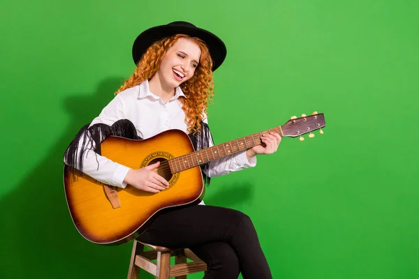 Portret van aantrekkelijk vrolijk getalenteerd meisje zitten op stoel spelen gitaar zingen hit geïsoleerd over helder groene kleur achtergrond — Stockfoto