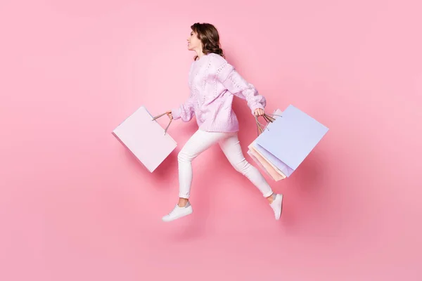 Повна довжина кузова профілю збоку гарна весела дівчина, що стрибає, несучи речі сумки ізольовані на рожевому пастельному кольоровому фоні — стокове фото