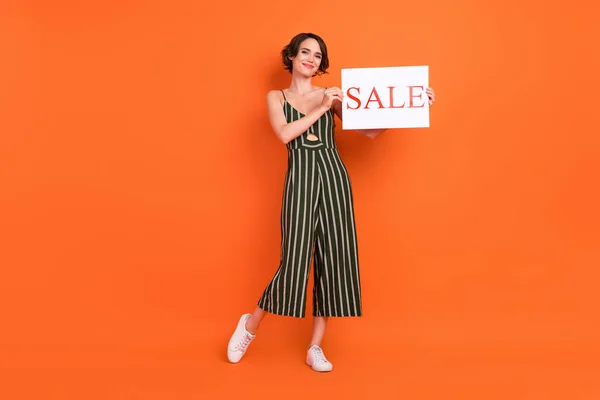 Foto in voller Größe von lustigen Brünette junge Dame stehen mit Poster tragen Gesamt Turnschuhe isoliert auf orangefarbenem Hintergrund — Stockfoto