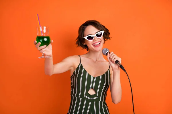 Foto de chica atractiva joven feliz sonrisa positiva fiesta bebida cóctel vítores tostadas micrófono aislado sobre fondo de color naranja — Foto de Stock