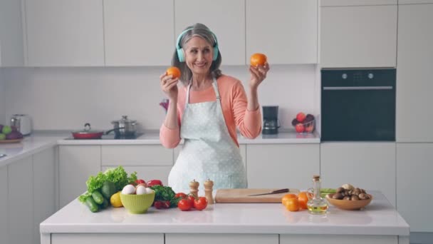 Весела радісна бабуся тримає два танець з апельсинами весело слухати навушники — стокове відео