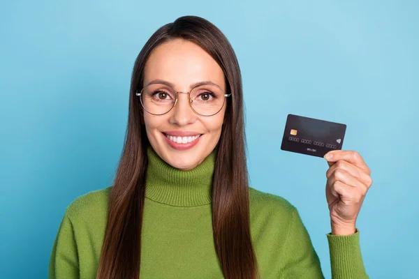 Fénykép csinos fényes fiatal nő visel zöld garbó szemüveg gazdaság bankkártya mosolygós elszigetelt kék szín háttér — Stock Fotó