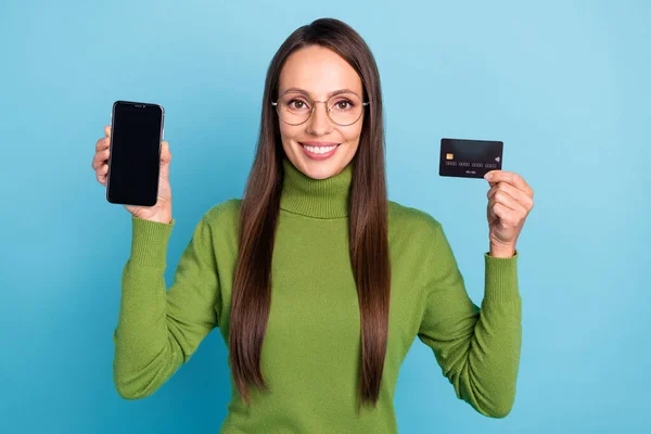 Foto av glänsande söt kvinna bära gröna polotröja glasögon hålla bankkort modern enhet tomt utrymme isolerad blå färg bakgrund — Stockfoto