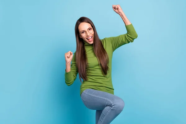 Foto de encantadora mujer joven afortunada usar gafas de cuello alto verdes sonriendo puños ascendentes aislado fondo de color azul —  Fotos de Stock