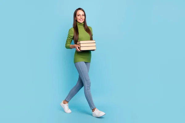 Photo of charming smart young woman wear green turtleneck glasses smiling walking holding book stos odizolowany niebieski kolor tła — Zdjęcie stockowe